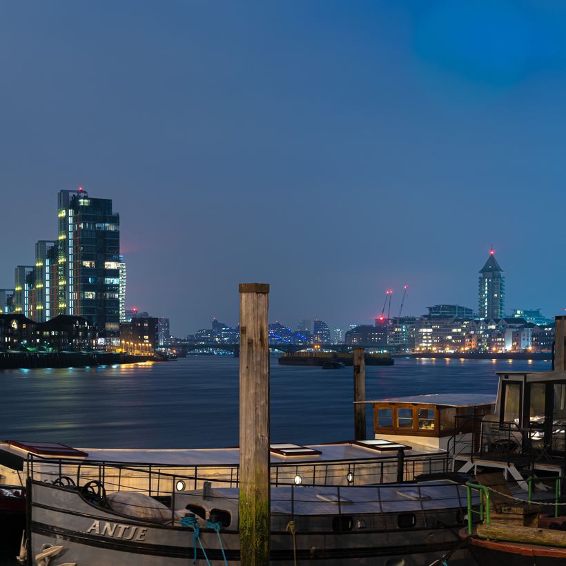 Moored barges on the river with a lit skyline at night