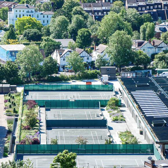 Aerial view over tennis courts and leafy suburban rooftops