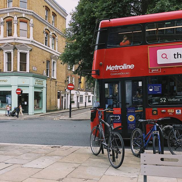 Red bus at corner shops with bikes on the pavement